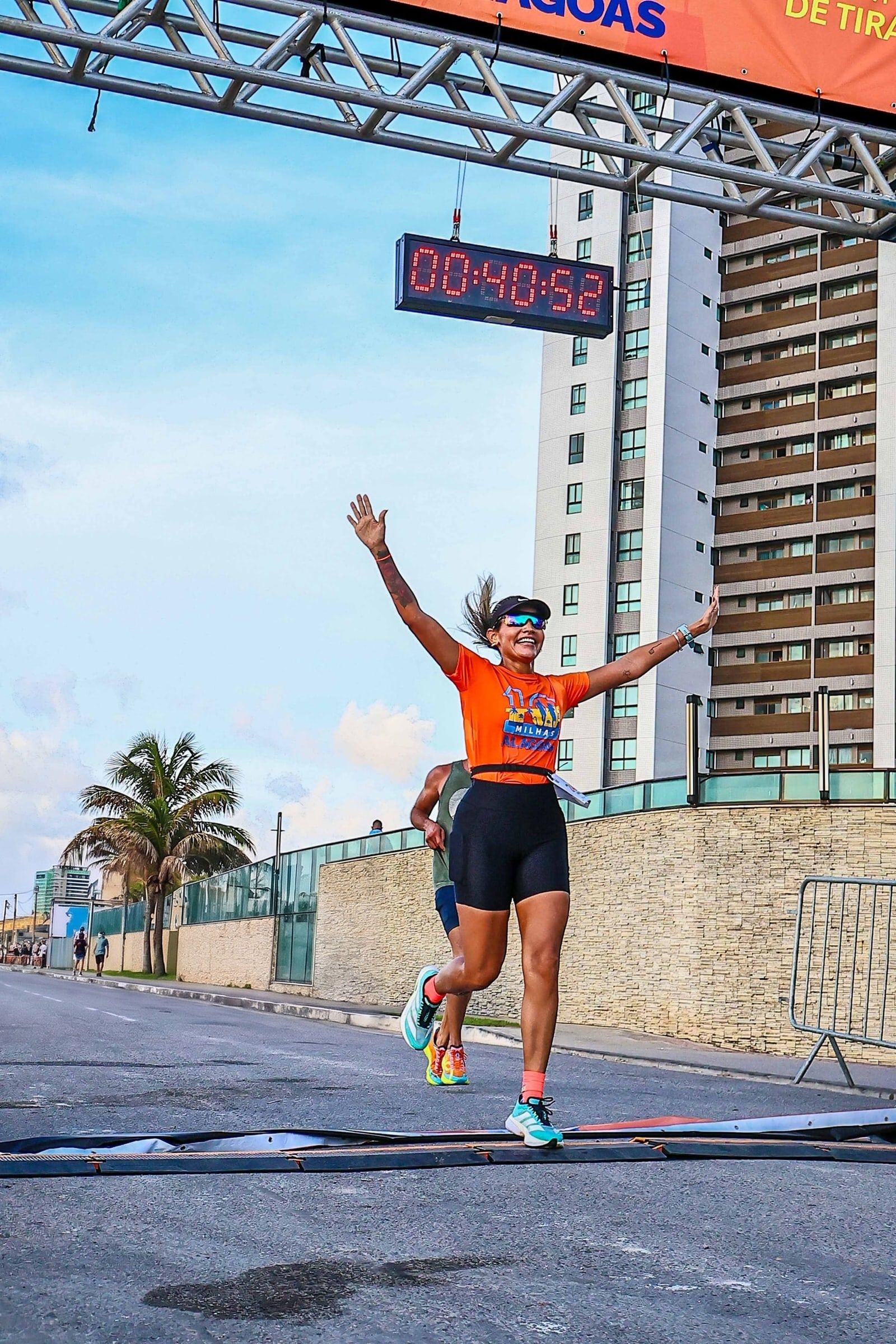 Atleta cruza a linha de chegada de braços abertos, com o cronômetro oficial ao fundo