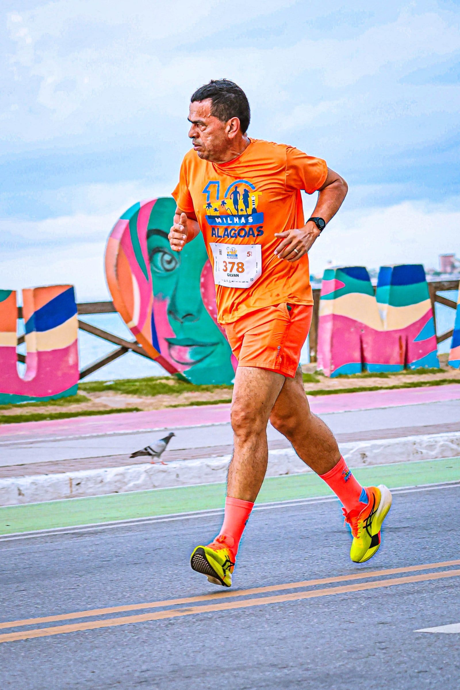 Corredor com a camisa oficial passando pelo letreiro colorido Eu Amo Maceió